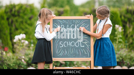 Glückliche kleine Schulmädchen mit einer Tafel im Freien Stockfoto