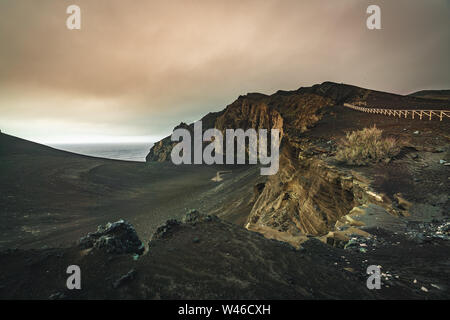 Blick über den Vulkan Capelinhos, Leuchtturm von Ponta Dos Capelinhos auf der westlichen Küste auf die Insel Faial, Azoren, Portugal mit einem dramatischen Sonnenuntergang und stark Stockfoto