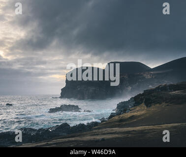 Blick über den Vulkan Capelinhos, Leuchtturm von Ponta Dos Capelinhos auf der westlichen Küste auf die Insel Faial, Azoren, Portugal mit einem dramatischen Sonnenuntergang und stark Stockfoto