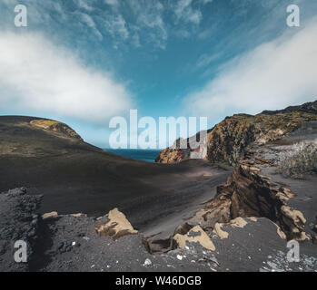 Blick über den Vulkan Capelinhos, Leuchtturm von Ponta Dos Capelinhos auf der westlichen Küste auf die Insel Faial, Azoren, Portugal an einem sonnigen Tag mit blauen Himmel und Stockfoto