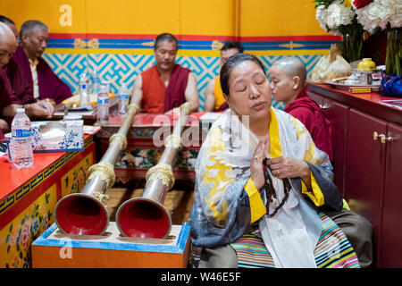 Ein frommer Nepalesischen Sherpa Buddhistischen betet und meditiert vor den Mönchen und die dungchen, die traditionelle buddhistische lange Horn. In Elmhurst Queens, NY Stockfoto