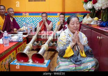 Ein frommer Nepalesischen Sherpa Buddhistischen betet und meditiert vor der Mönche spielen Der dungchen, die traditionelle buddhistische lange Horn. In Elmhurst Queens, NY Stockfoto