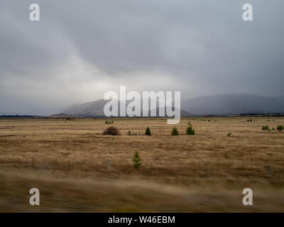 Herbst Grünland in Neuseeland Südinsel, mit Blick auf die ominöse Regen - Wolke bedeckte Berge in der Ferne, in der Nähe von Wanaka Stockfoto