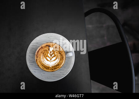 Graue Tasse frischen Cappuccino mit Schokolade auf Schaum auf dunklen Black Metal Tabelle Hintergrund. Leeren Platz für Text, kopieren. Kaffee sucht Konzept. Stockfoto