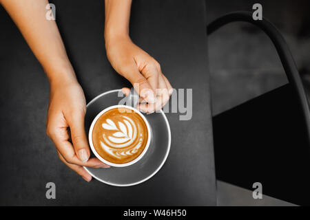 Tasse Cappuccino in der Frau die Hände auf dunklen Black Metal Tabelle Hintergrund. Leeren Platz für Text. Kaffee sucht. Blick von oben in den hipster Cafe. Stockfoto