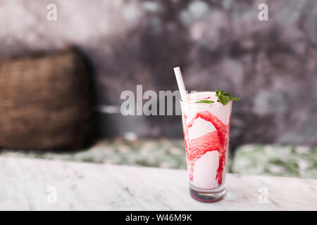 Frische leckere kalte Milch Shake mit roten Erdbeer Sirup auf weißem Marmortisch. Grauer Beton Hintergrund. Süße frappuccino trinken. Sommer trinken Stockfoto