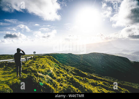 Junger Mann touristische mit Blick auf den wunderschönen Panoramablick von Lagoa do Fogo, See von Feuer, in Sao Miguel, Azoren, Portugal. Sonnigen Tag mit blauem Himmel Stockfoto