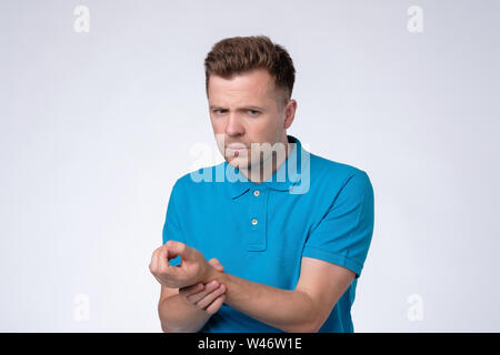 Junger Mann im blauen T-Shirt Hand am Handgelenk hält, überprüft Puls oder Herzschlag, kümmert sich um seine Gesundheit Stockfoto