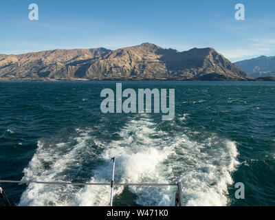 Schaumige Spur einer Bootsfahrt auf dem Lake Wanaka, mit blauem Himmel und Blick auf die Berge in der Ferne Stockfoto