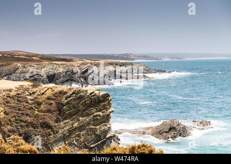 Ein unbekannter Mann steht in der Nähe einer Klippe mit Blick auf das Meer in der Ortschaft Porto Covo, Portugal Stockfoto