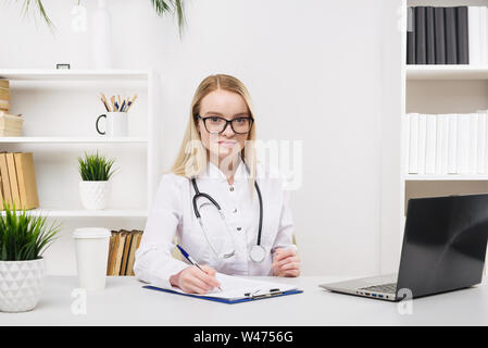 Junge schöne Arzt Frau glücklich und Lächeln im Krankenhaus, Sitzen am Tisch, medizinisches Konzept Stockfoto