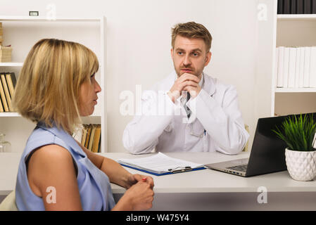 Junge Frau auf einer Beratung mit einem männlichen Arzt oder Therapeuten in seinem Büro. Selektiver Fokus auf den Arzt. Stockfoto