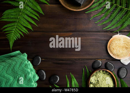 Green Spa Draufsicht mit Farnblätter auf hölzernen Hintergrund mit Kopie Raum, Massage Steine, grün Handtuch, lehmpulver Schüssel Stockfoto