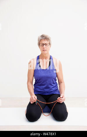 Reifer senior Frau practing Sanfte restorative Yoga in weißem Hintergrund fotografiert. Stockfoto