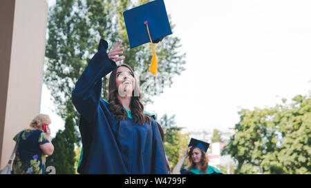 Hochschulabsolventen werfen Graduierung Hüte in der Luft. Gruppe der glücklichen Absolventen der akademischen Kleider in der Nähe der Universität. Junge Studenten Kleid Stockfoto