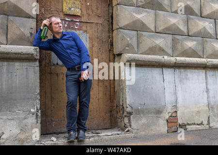 Ein betrunkener Mann steht in der Gasse mit einer Flasche alkoholische Getränk und nervös schaut auf Passanten Stockfoto