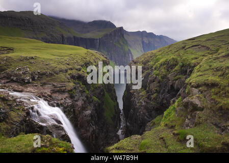 Wasserfall und Klippen am Ende der Fjallavatn, Insel Vágar, die Färöer Inseln, im Sommer Stockfoto