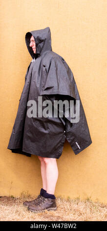 Festival goer in großen wasserdicht Kap Unterschlupf vor dem Regen, Latitude Festival, henham Park, Suffolk, Großbritannien am 20. Juli 2019 Stockfoto