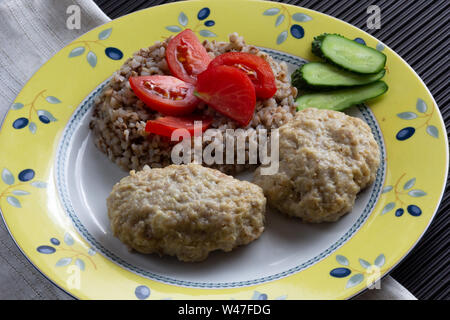 Gekochten Buchweizen und Frikadellen auf der Platte durch die Tomate und Gurke eingerichtet Stockfoto