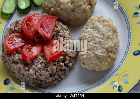 Gekochten Buchweizen und Frikadellen auf der Platte durch die Tomate und Gurke eingerichtet Stockfoto
