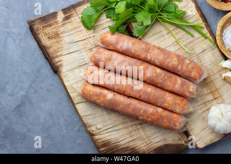 Raw nicht gegartem Fleisch Wurst und grüne Kräuter auf einem Holzbrett. Stockfoto