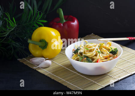 Asiatische Küche, Braten udon Nudeln mit Gemüse und Sojasauce auf einem Bambus matte Rühren, schwarzer Hintergrund, asiatische Küche Stockfoto