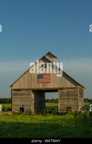 Alte hölzerne Scheune im Mittelwesten mit amerikanischen Flagge am Nachmittag. LaSalle County, Illinois, USA Stockfoto