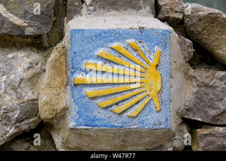 Traditionelle Markierung entlang des Camino del Norte im Dorf Cuerres. Die Jakobsmuschel und der gelbe Pfeil sind allgegenwärtig Symbole der Wallfahrt Stockfoto