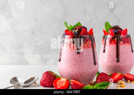 Zwei Gläser Erdbeer Joghurt oder Chia Samen Pudding mit Schokolade, frische Beeren und Minze für gesundes leckeres Frühstück auf Weiß konkreten Hintergrund Stockfoto
