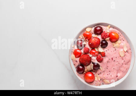 Rosa smoothie Schale mit frischen Beeren, Nüsse und Samen auf weißem Marmortisch. gesundes Frühstück. Ansicht von oben mit der Kopie Raum Stockfoto