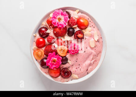 Rosa smoothie Schüssel oder schöne Creme mit frischen Beeren, rosa Blüten, Nüsse und Samen auf weißem Marmortisch. gesundes Frühstück. top View Stockfoto