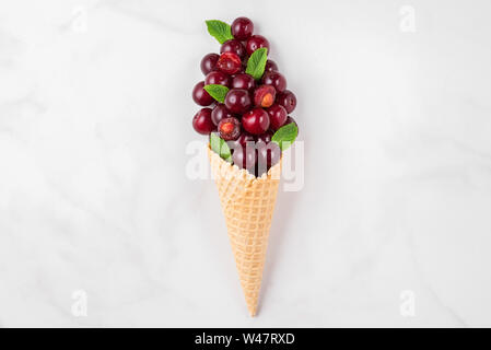 Sommer cherry Beeren mit Minze im Waffle Kegel auf weißem Hintergrund. Sommer essen Konzept. top anzeigen. Flach Stockfoto