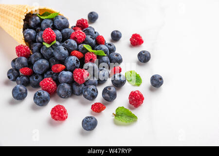 Wilde Beeren Heidelbeere, Erdbeere und Himbeere mit Minze in Waffel Eiswaffel auf weißem Hintergrund. Sommer essen Konzept. Nach oben Schließen Stockfoto