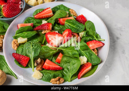 Salat mit Erdbeeren, Spinatblätter, Parmesan und Walnüsse auf konkreten Hintergrund. gesunde Ernährung Lebensmittel. Nach oben Schließen Stockfoto