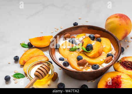 Griechischer Joghurt mit Pfirsichen, Hafer, Blaubeeren, Honig und Minze in eine Schüssel für gesundes Frühstück auf weißem Hintergrund. Nach oben Schließen Stockfoto