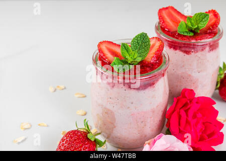 Gesunde Ernährung Frühstück Dessert. Erdbeere über Nacht Hafer mit frischen Beeren und Minze mit rose Blumen auf weißem Marmor tisch. Nach oben Schließen Stockfoto