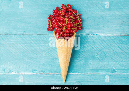 Rote Johannisbeere Beeren in der Waffel Eiswaffel auf Blau Holz- Hintergrund. Kreative Sommer essen Konzept. Flach. top View Stockfoto