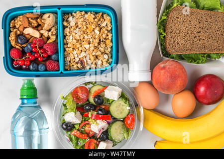 Mittag- Boxen mit gesunden Lebensmitteln Weg für den ganzen Tag nehmen. Frühstück Müsli mit Joghurt, griechischer Salat, Sandwich, Obst und Gemüse mit Wasser. nach oben Stockfoto