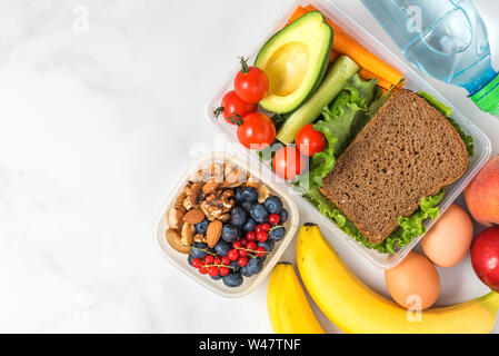 Mittag- Boxen mit Essen fertig für die Arbeit oder in die Schule zu gehen. Sandwich, Gemüse, Avocados, Nüsse, Beeren, Eiern und Wasser. die Vorbereitung von Mahlzeiten oder Diäten anhand von quantitativen Simulatio Stockfoto