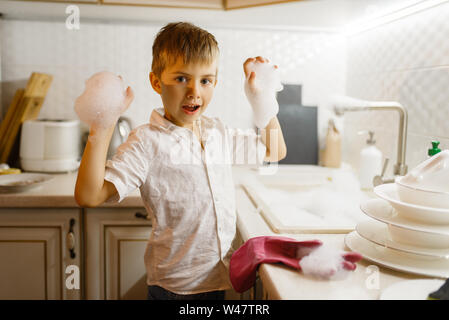 Ein kleiner Junge in Handschuhe beim Abwasch in der Küche. Baby Hausarbeit zu Hause. Helfer des jungen Mama reinigt das Haus Stockfoto