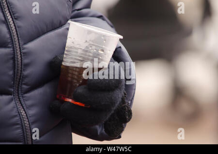 Behandschuhten Hand eine Schale aus Kunststoff mit Tee. Street Food im Winter. Stockfoto