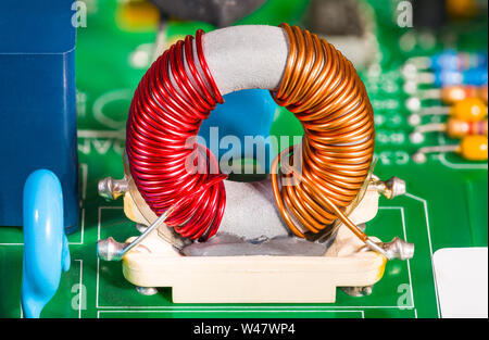 Ringkerntrafo Spule. Bunte Kupferdraht Wicklung auf Spule mit Ferritkern. Elektronische Komponenten auf der grünen Platine. Wechselrichter close-up. Stockfoto