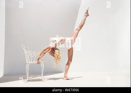 Klassische Schönheit in Yoga rad Pose oder nach oben Bug Haltung unter Verwendung einer schönen Stuhl als Stütze. Diese Frau ist eine Ballerina gedreht Yogi. Stockfoto