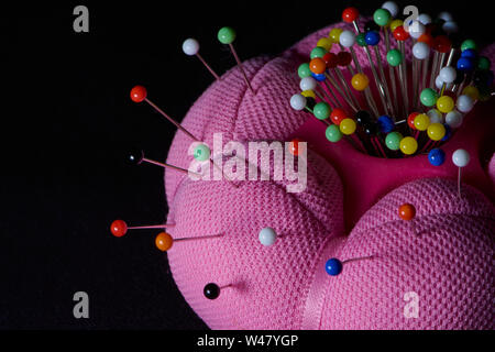 Rosa Nadel Kissen mit einer Menge farbige Stifte in es, horizontal Farbe Makro Foto auf schwarzem Hintergrund Stockfoto