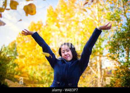 Asiatische Jugendmädchen werfen bis gelbe Blätter im Park mit Bäumen wechselnden Farben im Herbst Saison. Stockfoto