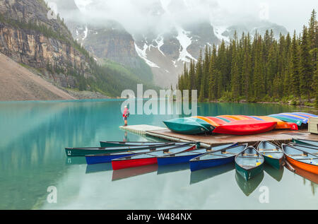 Bunte Kanus und ein Besucher am Moraine Lake, Banff National Park, Kanada, auf einem Regen Morgen Stockfoto