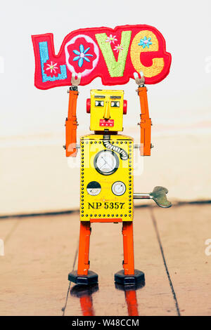 Retro gelb Roboter mann Halten eines hellen und bunten Tuch liebe Zeichen, stehend auf einem alten Holzboden Stockfoto