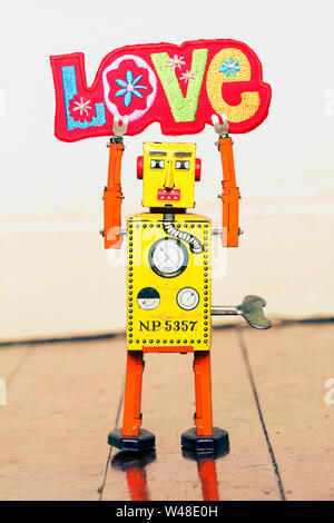 Retro gelb Roboter mann Halten eines hellen und bunten Tuch liebe Zeichen, stehend auf einem alten Holzboden Stockfoto