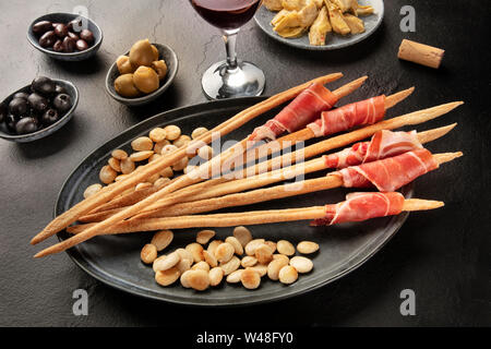 Italienische Antipasti. Schinken eingewickelten Italienische Grissini mit Oliven, Artischocken, und Wein auf schwarzem Hintergrund Stockfoto