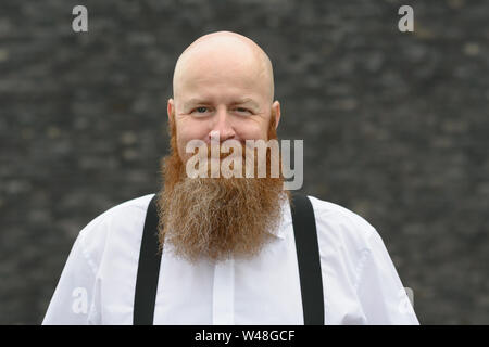 Balding bärtigen rothaarigen Mann mit einem freundlichen Lächeln das Tragen von Zahnspangen vor einem grauen Hintergrund in einer Nahaufnahme, Porträt Stockfoto